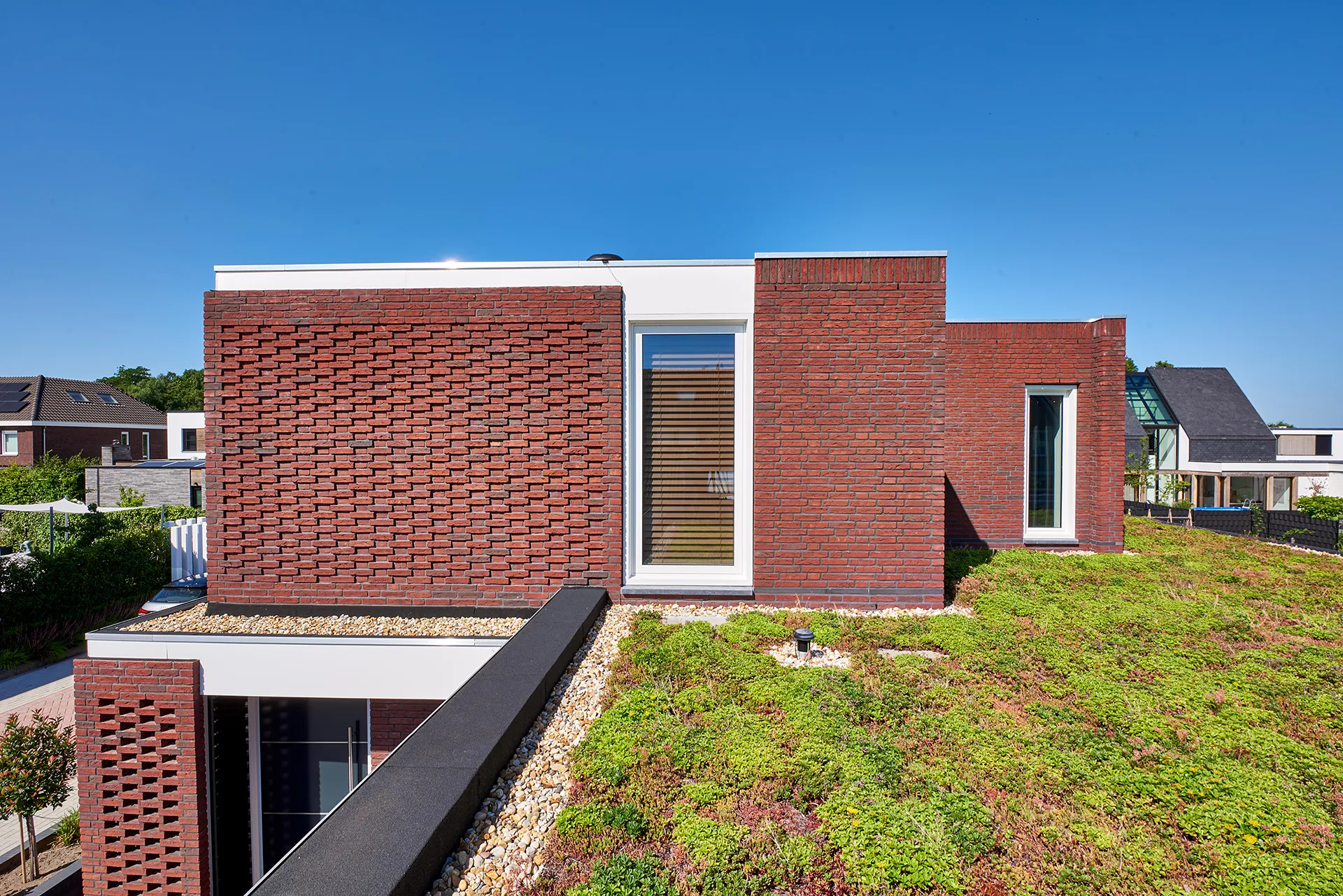 Woning met witte dakranden, groendak en metselwerk in vlaams verband met terugliggende koppen.