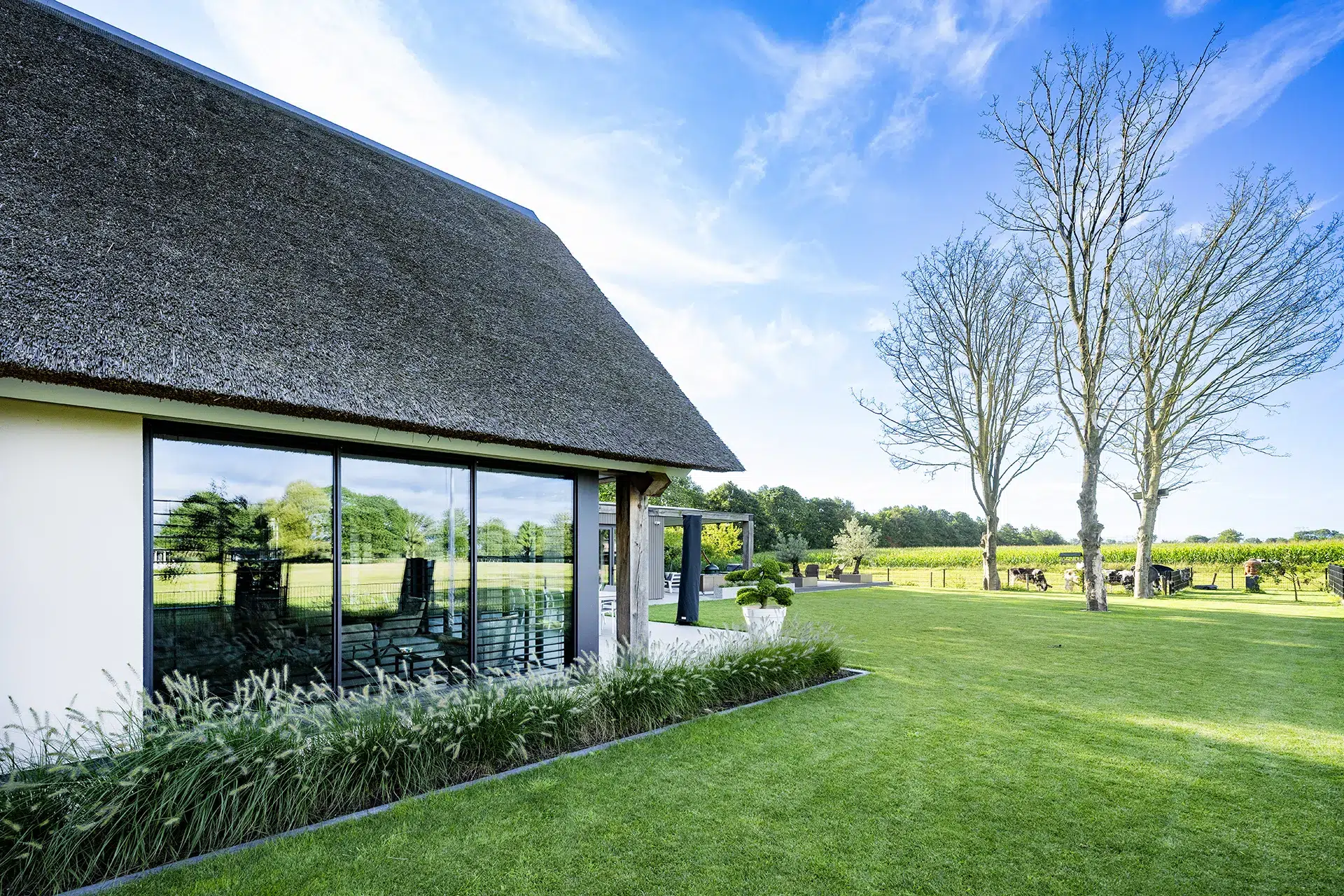 Zijgevel met grote pui voor weids uitzicht vanuit wit gestucte villa met rieten kap in Sprang-Capelle.