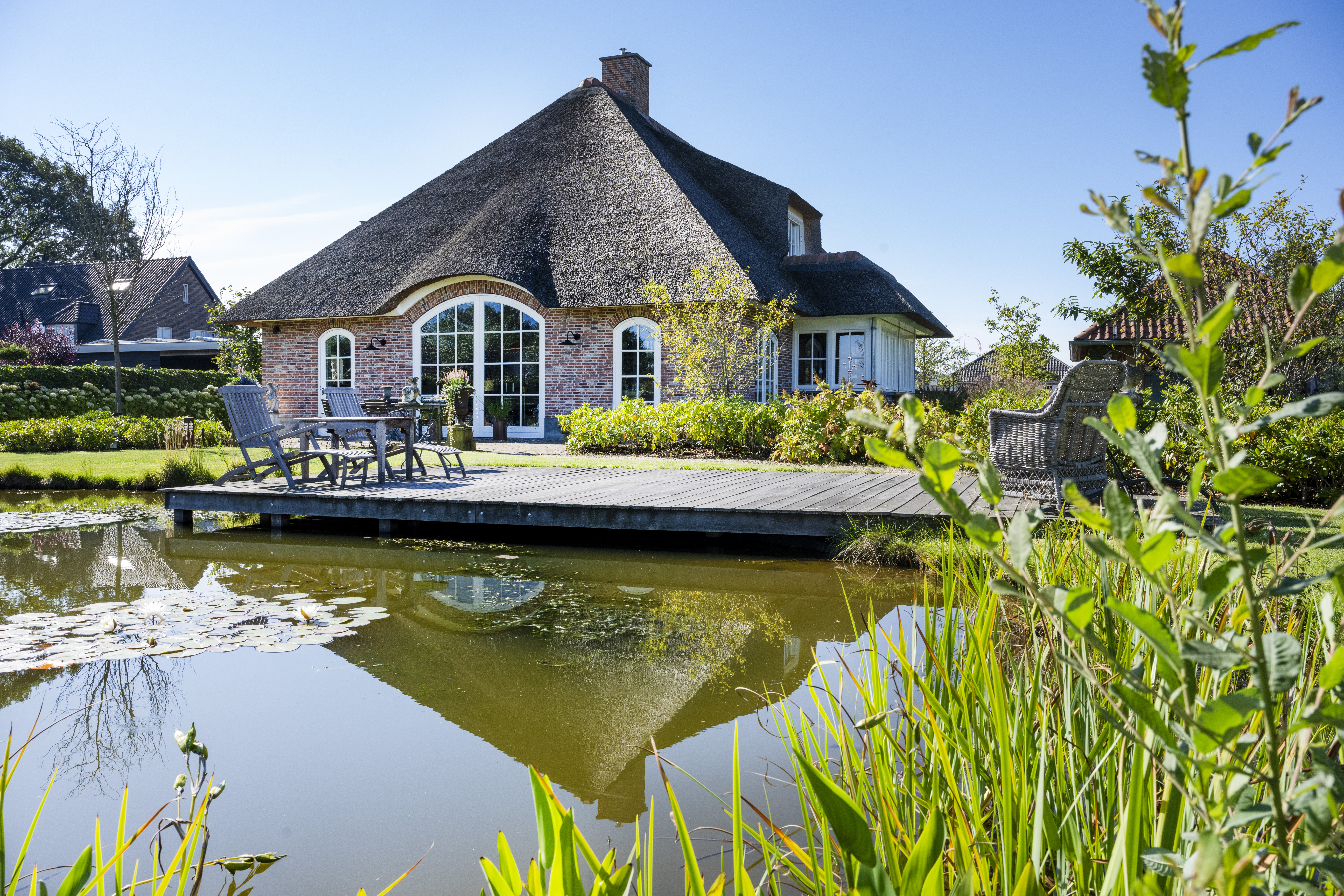 Reflectie van landelijke woning met rieten kap in vijver.