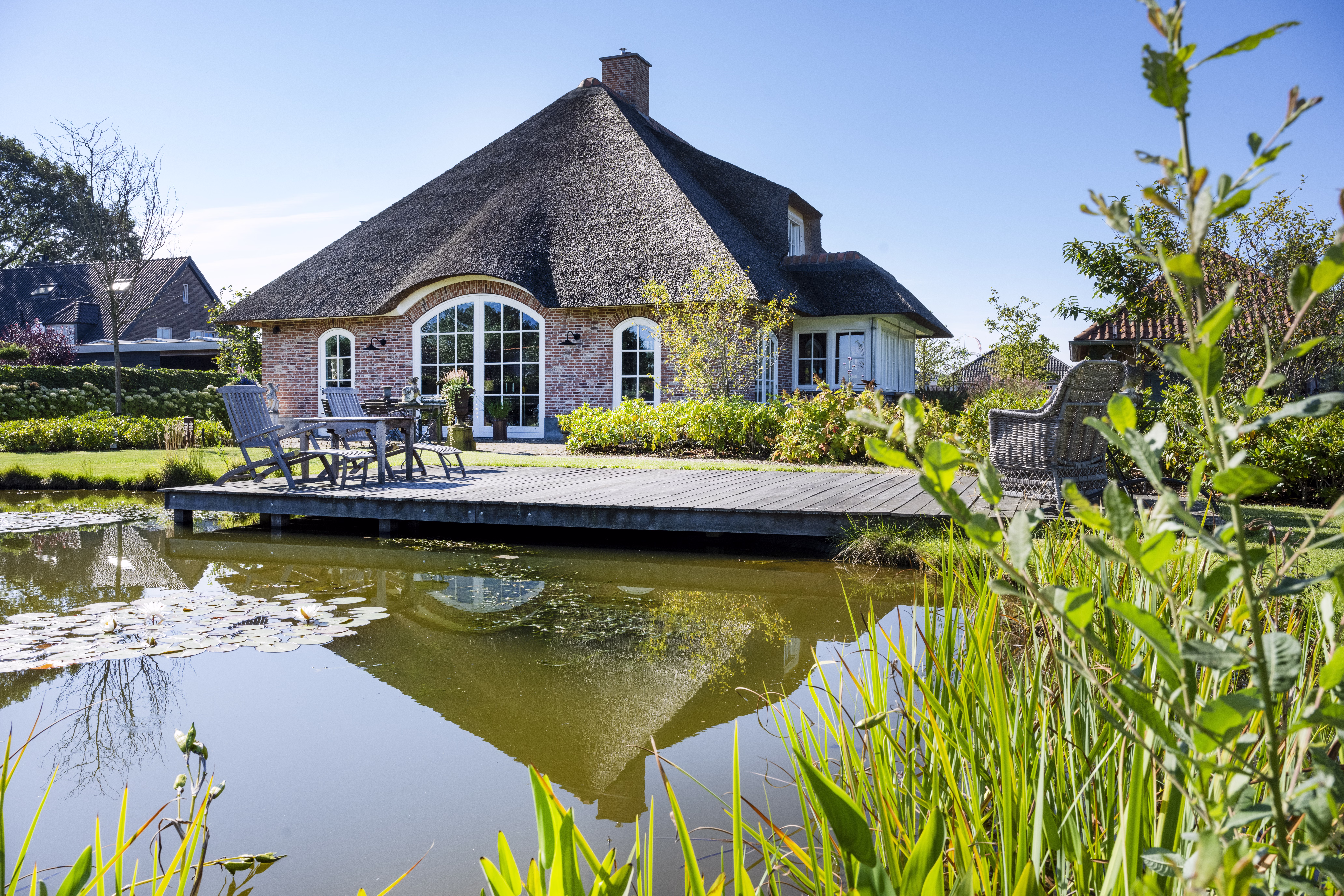 Reflectie van landelijke woning met rieten kap in vijver.