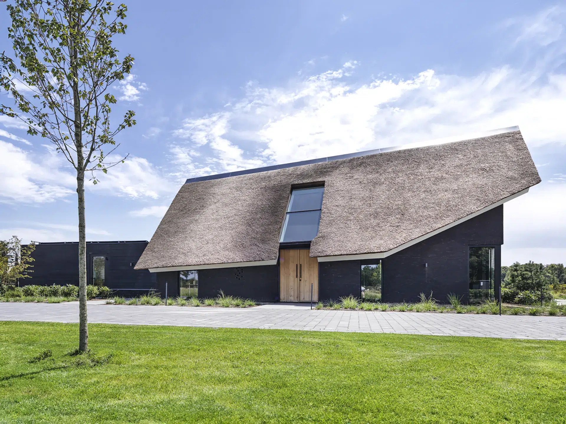 Voorgevel van woning met schuine rieten kap, donker metselwerk en houten voordeur in Kaatsheuvel nabij de Loonse en Drunense duinen.