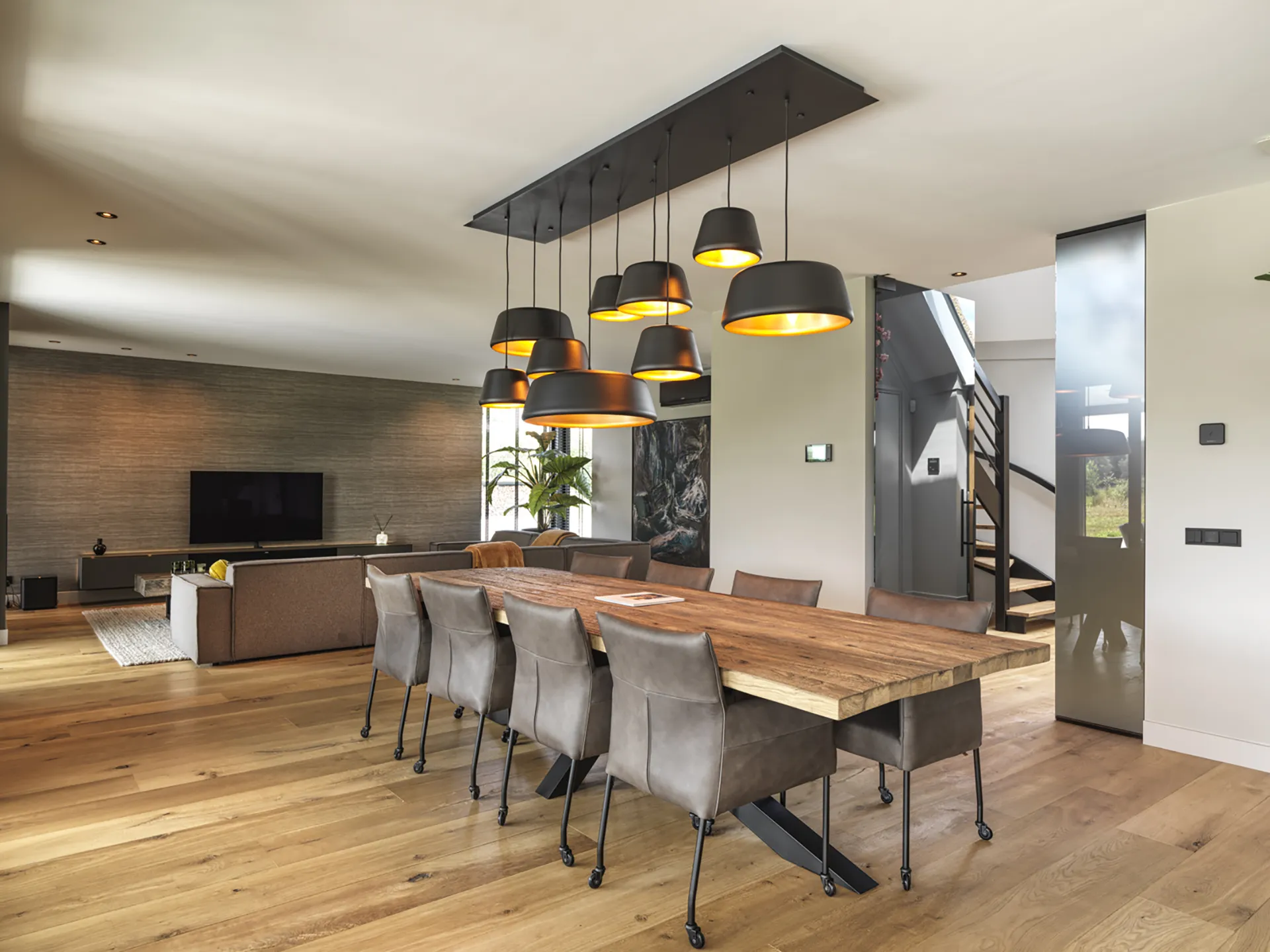 woon en eetkamer met houten eettafel en bruin lederen stoelen en moderne taatsdeuren naar entree toe.
