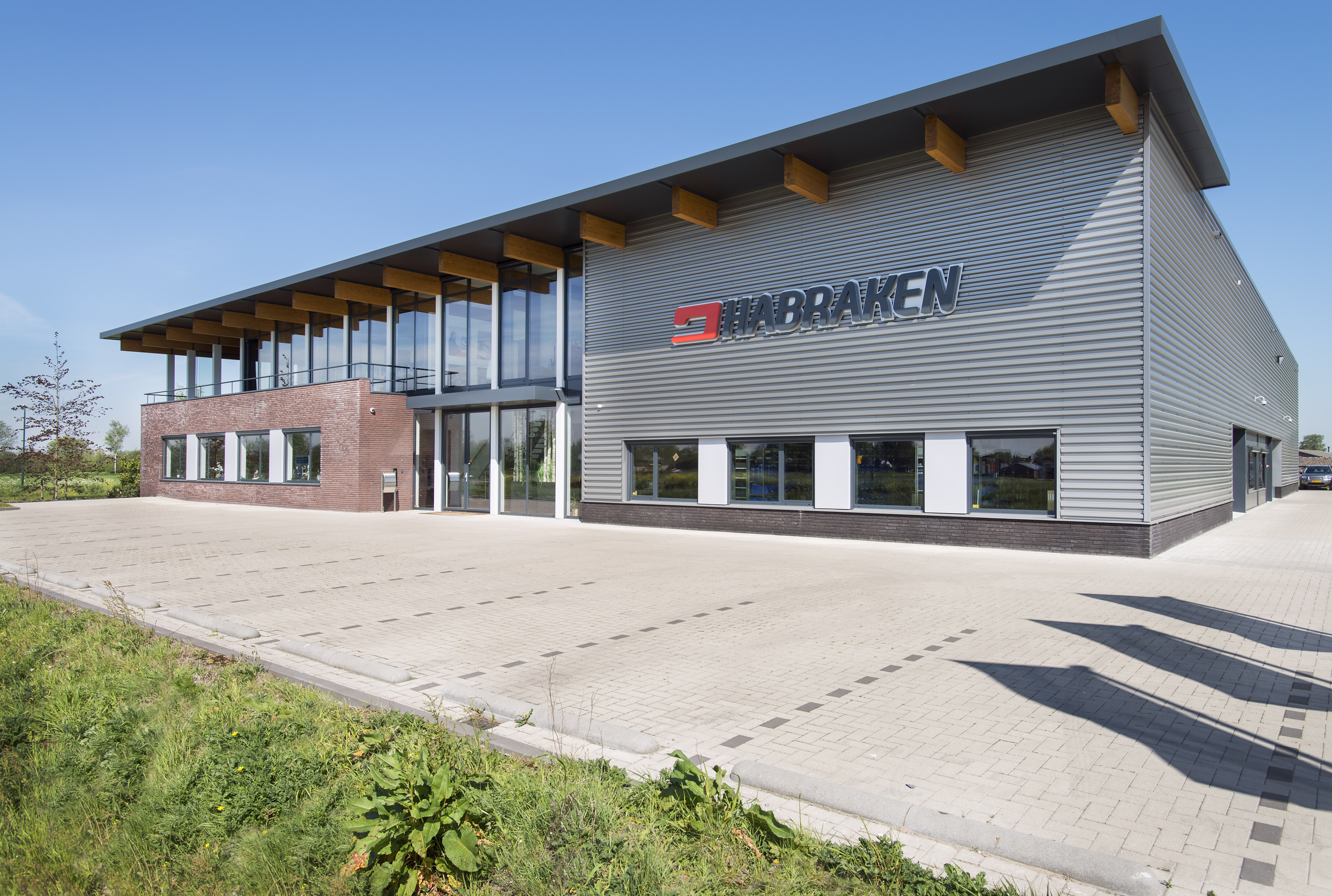 Kantoorgevel met gelamineerd houten overstek dat de grote raampartijen beschermt tegen directe zoninstraling.